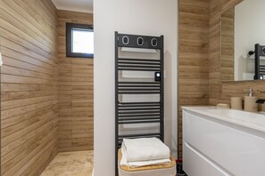 Ein modernes Badezimmer mit Holzwandverkleidung, einem schwarzen Handtuchhalter, einem weißen Waschbecken und einem Spiegel.