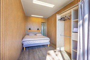 Ein Schlafzimmer mit Bett, Holzwandverkleidung, einem Schrank mit Platz zum Aufhängen und einer Tür zu einem anderen Raum.