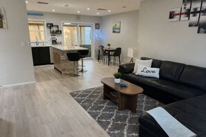 Een moderne woonkamer met een zwarte leren bank, een salontafel, en een eethoek met een keuken op de achtergrond.