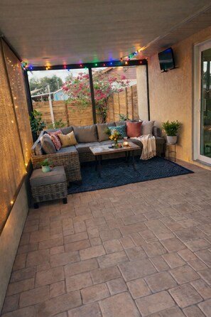 A covered patio with a sofa, small table, and potted plants. - The Cozy Coastal Retreat with screened patio and arcades (Sarasota)
