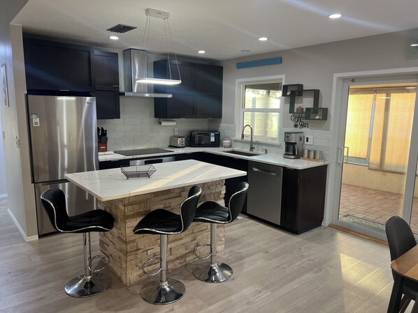A modern kitchen with a central island, bar stools, stainless steel appliances, and a view to the outside. - The Cozy Coastal Retreat with screened patio and arcades (Sarasota)