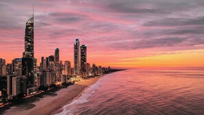 A coastal cityscape with high-rise buildings, a beach, and a sunset sky. - Residence Surfers Ocean and Pool Views (Surfers Paradise)