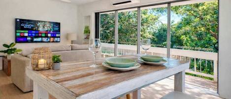 A modern living room with a wooden dining table, green plates, and a TV displaying a movie.