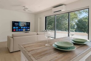 Una sala de estar moderna con un sofá, una mesa de centro de madera, un televisor montado en la pared y un balcón con puerta de cristal.