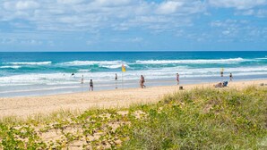 A beach with people walking and sitting, a flag, and the ocean. - Ocean View Studio 2 Beds Free WI-FI (Surfers Paradise)