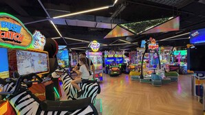 An indoor arcade with various gaming machines, including a racing game and claw machines. - L17 Spacious Central 2BR Wi-Fi (Surfers Paradise)