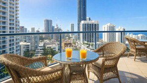 A balcony with wicker furniture, a glass table, and two glasses of orange juice. - L17 Spacious Central 2BR Wi-Fi (Surfers Paradise)