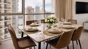 A dining room with a large window, a table set for four, and a city view. - L17 Spacious Central 2BR Wi-Fi (Surfers Paradise)