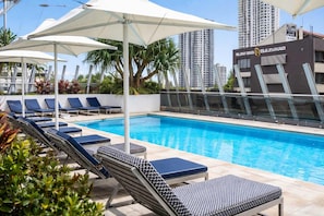 A swimming pool with lounge chairs and umbrellas, surrounded by tall buildings. - Level 13 Ocean View Retreat (Surfers Paradise)