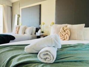 Une chambre d’hôtel avec deux lits, une couvre-lit verte et des serviettes blanches roulées.