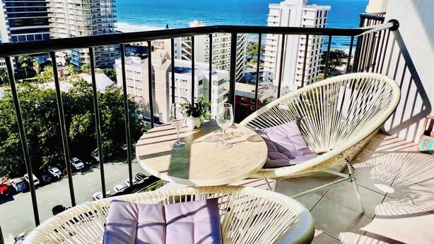 A balcony with wicker furniture, a round table, and a view of the ocean and cityscape. - Ocean View studio 2 Beds, Free Wi-Fi (Surfers Paradise)