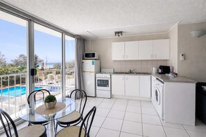 A modern kitchen with white cabinets, a microwave, an oven, and a washing machine. There's a glass table with chairs, and a balcony with a view of the sea. - Surfers Beachside Studio Ocean View (Surfers Paradise)
