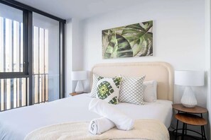 A hotel room with a bed, pillows, a wall art piece, a window, and a nightstand with a lamp. - Family Paradise in Surfers: BBQ&Pool (Surfers Paradise)