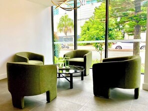 A modern room with three green armchairs, a glass coffee table, and large windows offering a view of the street and greenery outside. - Family Paradise in Surfers: BBQ&Pool (Surfers Paradise)