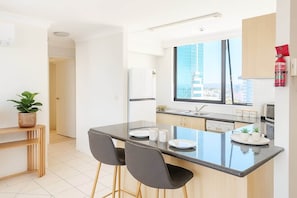 A modern kitchen with a central island, a dining area, and a view of the city. - Ocean Getaway 1BR Heated Pool & Netflix (Surfers Paradise)