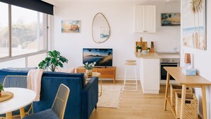 Ein modernes Wohnzimmer mit einem blauen Sofa, einem Esstisch und einer Küchenzeile mit weißen Schränken und einer Holz Arbeitsplatte.
