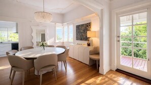 Une pièce comprenant une table à manger, des chaises, un lustre, un canapé, une fenêtre et une porte donnant sur l’extérieur.
