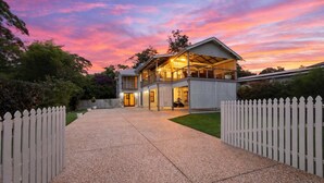 Une maison à deux étages avec un patio couvert, une allée et une clôture blanche en bois.