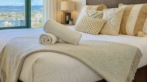 A hotel room with a large bed, a nightstand, a lamp, and a view of a cityscape through a large window. - L19 Ocean View Studio Near Beach Mantra Legends (Surfers Paradise)