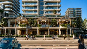 Een hotel met meerdere verdiepingen, balkons, een surfclub en een straat ervoor.