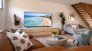 Een woonkamer met een grote flatscreen televisie, een bank, een salontafel en een trap.