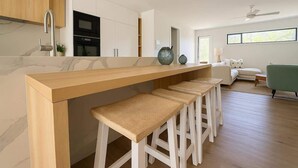 Een moderne keuken met een marmeren aanrechtblad, witte kasten en een bar voorzien van barkrukken.