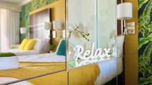 A hotel room with a bed, a glass partition with the word 'Relax' on it, and a view of another room with a bed and a window. - L15 Ocean View Suite with 2 Beds (Surfers Paradise)
