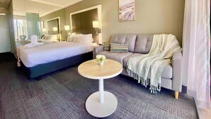 A hotel room with a bed, a sofa, a round table, and a painting on the wall. - High Floor King Studio Surfers (Surfers Paradise)