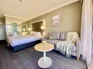 A hotel room with a bed, a sofa, a round table, and a painting on the wall. - High Floor King Studio Surfers (Surfers Paradise)