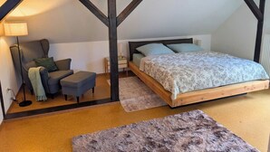 Een slaapkamer met een schuine plafond, een bed, nachtkastje, lamp, stoel en vloerkleed.