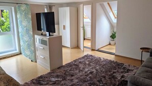 Een moderne woonkamer met een flatscreen televisie, een groot pluizig vloerkleed en een plafondlamp.