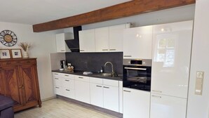 Een moderne keuken met witte kasten, een inbouwoven en een houten plafondbalk.