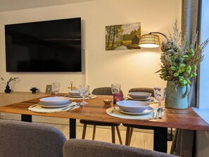 A dining area with a wooden table set for four, a flat-screen TV mounted on the wall, and a painting above the table. - Hofidyll Burg - 75-square-meter (DHH) apartment in a central yet quiet location in Burg (Spreewald) (Burg (Spreewald))