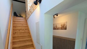Een houten trap met een lamp erboven, een radiator en een aan de muur hangend schilderij.