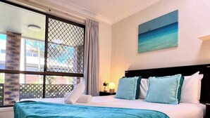Een hotelkamer met een bed, nachtkastje, raam met uitzicht en een schilderij aan de muur.