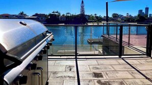 Een balkon aan het water met een barbecue, uitzicht op het water en een stadsbeeld op de achtergrond.