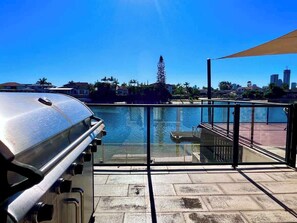 Ein Balkon am Wasser mit Grill, Blick auf das Wasser und einer Stadtlandschaft im Hintergrund.