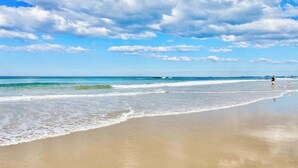 A beach with a wide sandy shore, gentle waves, and a clear sky with scattered clouds. - Family apartment in Surfers Paradise (Surfers Paradise)