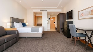 Ein Hotelzimmer mit einem Bett, einem Schreibtisch, einem Stuhl, einem Fernseher und einer Tür zu einem Badezimmer.
