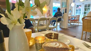Una mesa de comedor con una taza de café amarilla, una porción de pastel y un florero con flores blancas.
