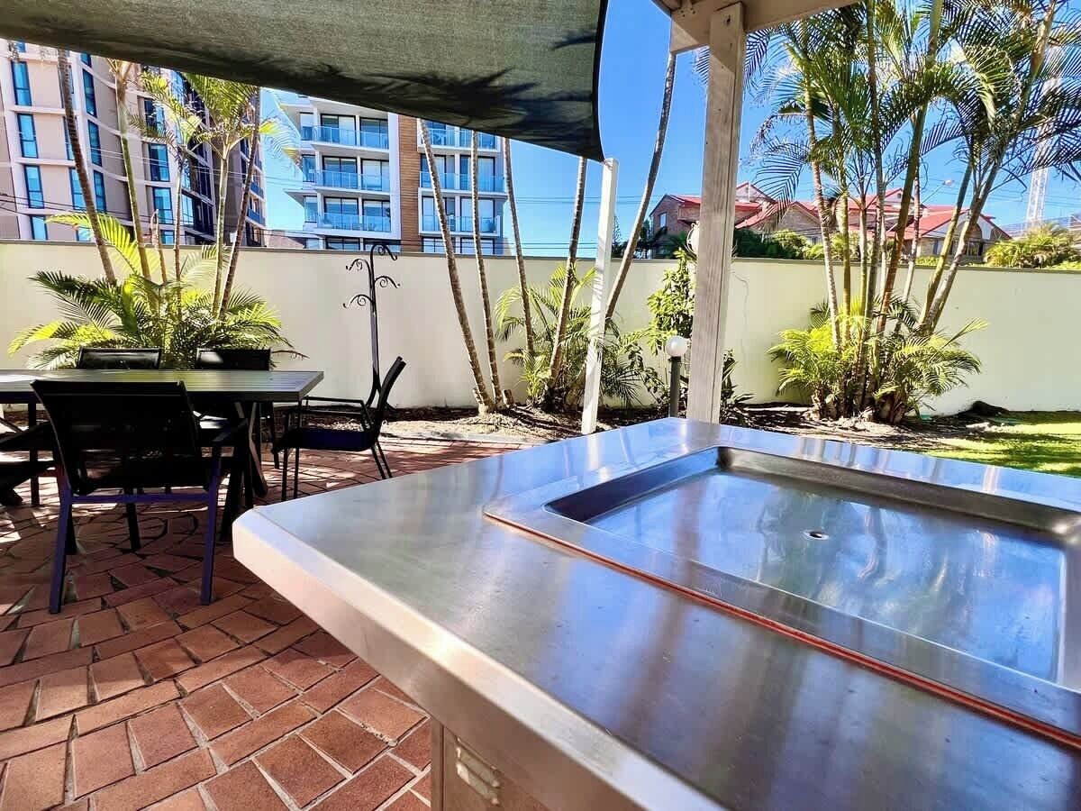Um espaço ao ar livre com mesa e cadeiras de metal, uma pequena piscina e vista para edifícios ao fundo.