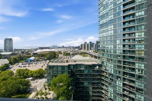 A high-rise building with a modern glass facade, a parking lot, and a stadium in the background. - Modern 1BR Downtown Condo w/ Private Balcony Views (Toronto)