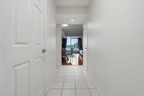 A hallway with white doors, a tiled floor, and a view of a balcony with a table and chairs. - Modern 1BR Downtown Condo w/ Private Balcony Views (Toronto)