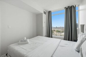 A hotel room with a large bed, a window with curtains, and a view of the cityscape. - Modern 1BR Downtown Condo w/ Private Balcony Views (Toronto)
