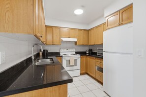 A kitchen with wooden cabinets, a white stove, a black countertop, and a white refrigerator. - Modern 1BR Downtown Condo w/ Private Balcony Views (Toronto)