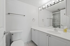A modern bathroom with a toilet, a sink, and a mirror with lights. - Modern 1BR Downtown Condo w/ Private Balcony Views (Toronto)