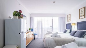 A hotel room with a bed, a desk, a chair, a trash bin, and a window with curtains. - Top level Ocean View Oasis: 3-Bed&Free Wi-Fi (Surfers Paradise)