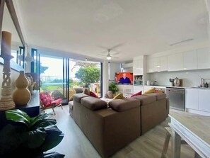 A modern living room with a brown sofa, a dining table, and a kitchen area with white cabinets. - Ocean front 1-bedroom apartment near Beach (Surfers Paradise)