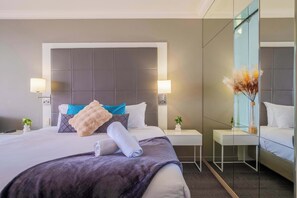A modern hotel room with a large bed, two bedside tables, a mirror, and a small plant. - L21 Ocean View Studio: King bed (Surfers Paradise)