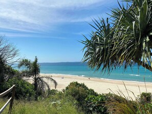 A beach with clear skies, a sandy shore, and some greenery in the foreground. - Ocean View 1BR Steps to Beach (Surfers Paradise)